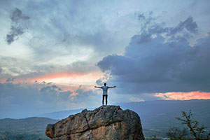 man with open arms on top of a mountain